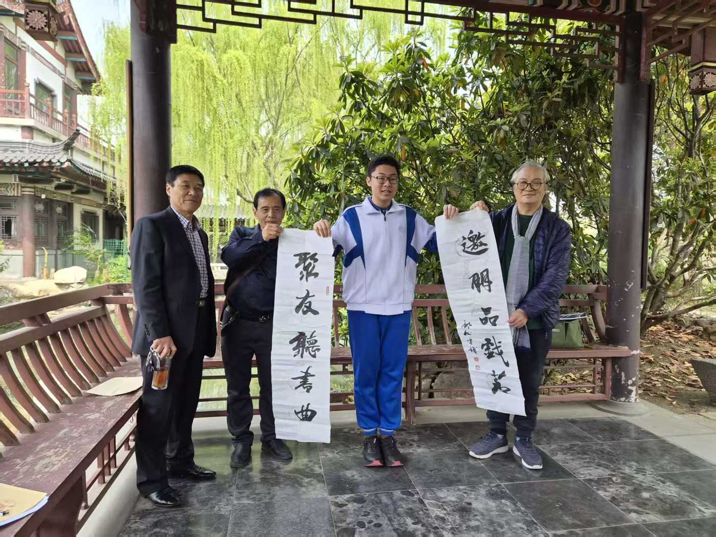 Ronghao Yang with three retired experts holding calligraphy scrolls at a Daming Lake pavilion
