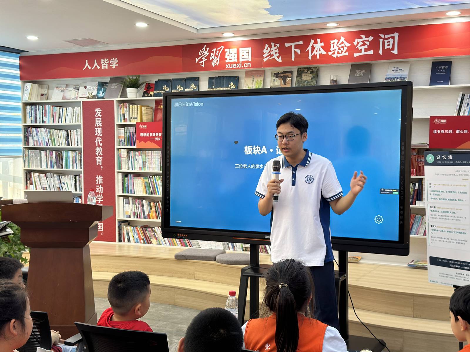 Ronghao Yang explaining the Wall of Memory exhibition panel to young visitors