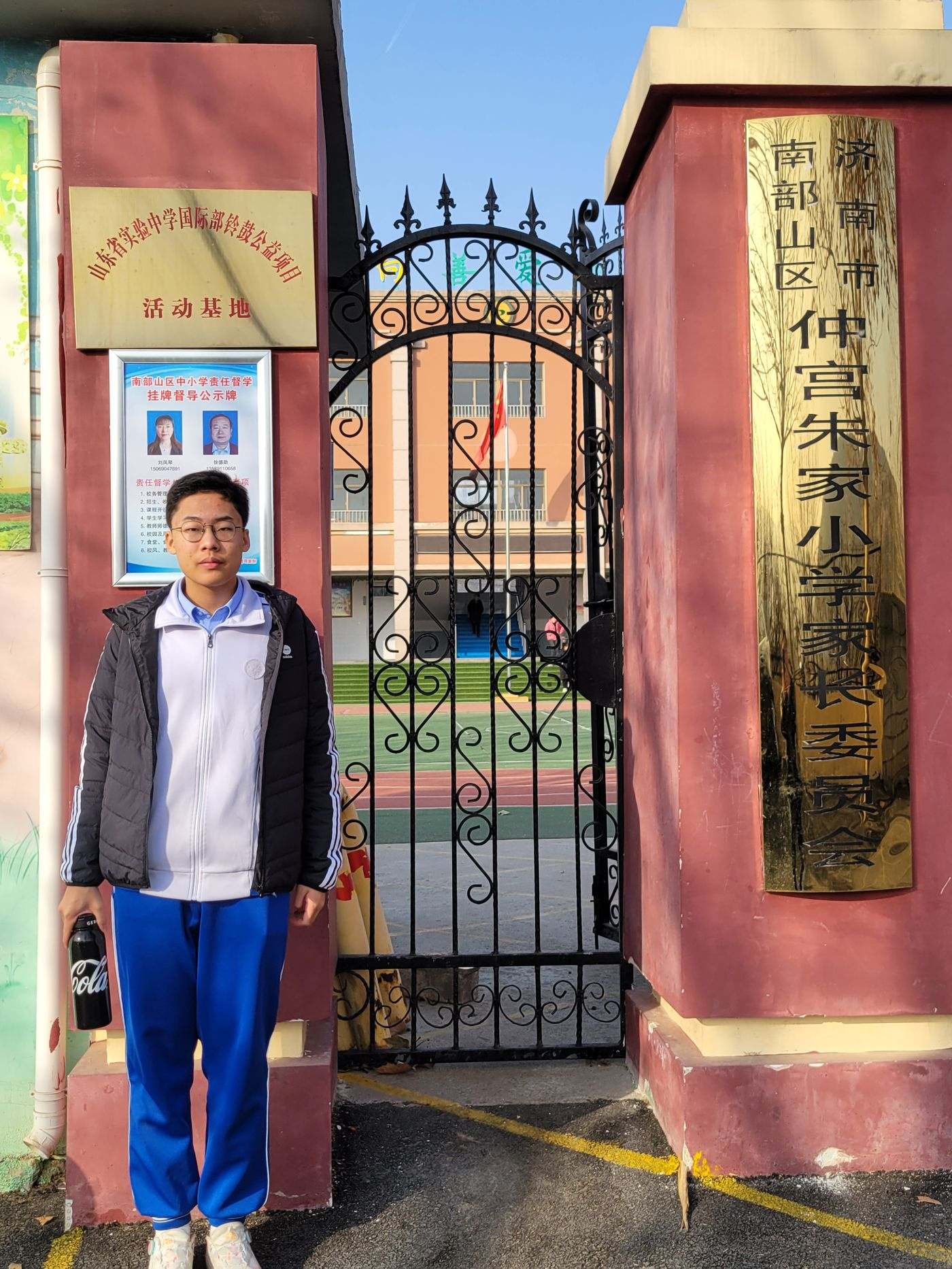 Ronghao Yang at the gate of Zhujia Primary School beside the official activity base plaque