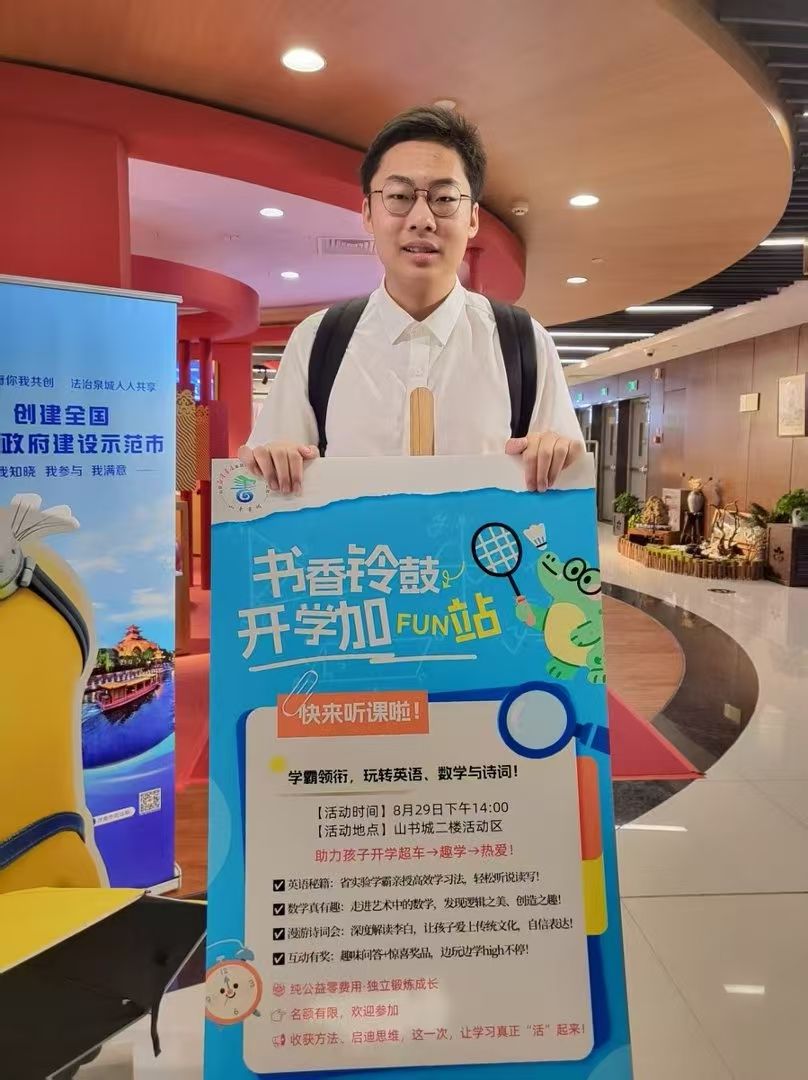 Ronghao Yang holding the Shuxiang Tambourine Back-to-School Fun Station signboard at Shandong Book City