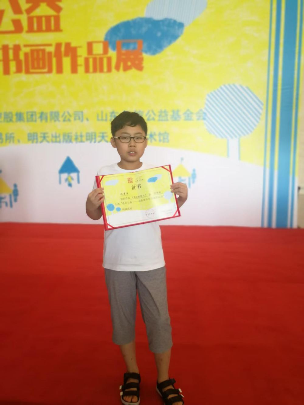 Young Ronghao holding a certificate at a charity painting exhibition as a child